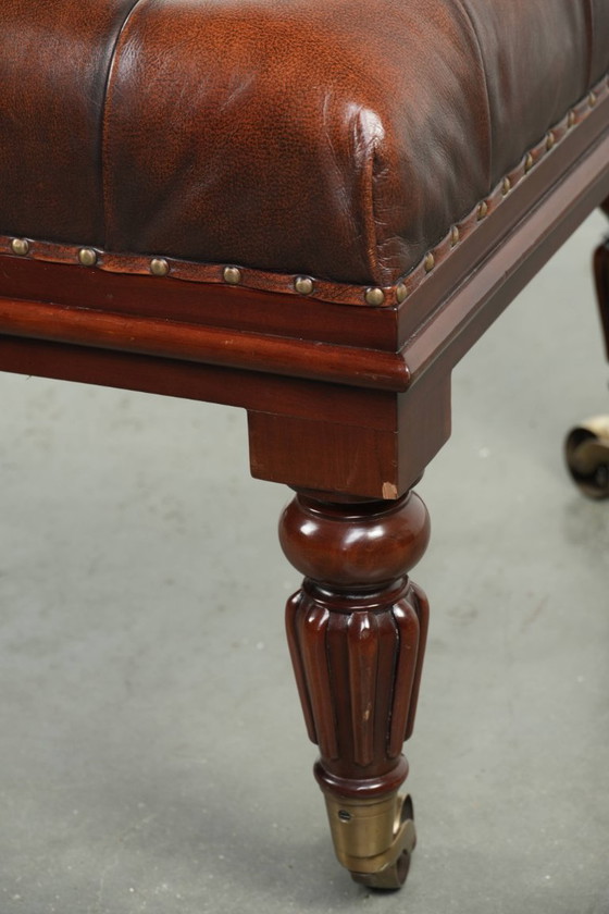 Image 1 of Grote bruine rundleren chesterfield hocker in Engelse stijl met sierlijke poten en messing wieltjes