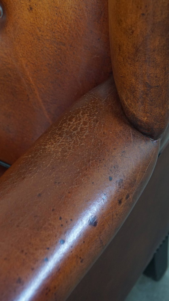 Image 1 of Schapenleren oorfauteuil met een warme kleurstelling en een afwerking met siernagels en zwarte biezen