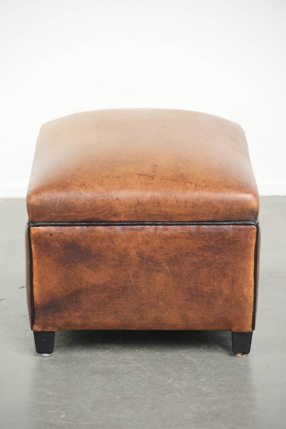 Image 1 of Characterful sheepskin footstool/ottoman with a beautiful patina and finished with black piping.
