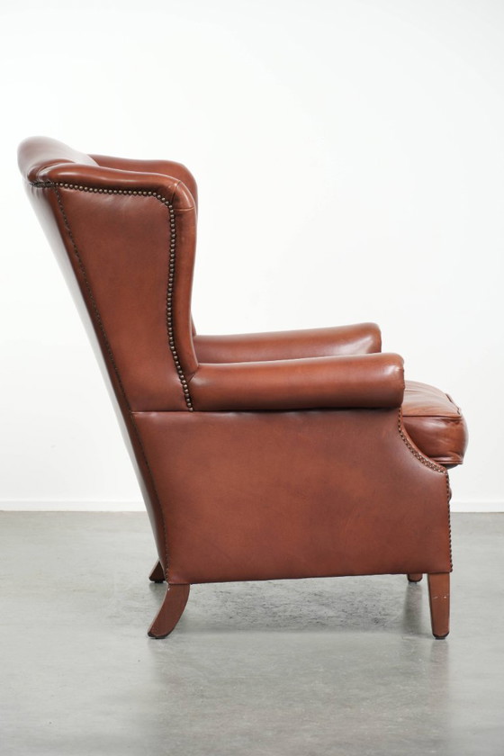 Image 1 of Comoda poltrona a orecchioni in pelle bovina color cognac in stile inglese.