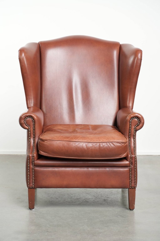 Cómodo sillón orejero de piel de vacuno color coñac al estilo inglés.