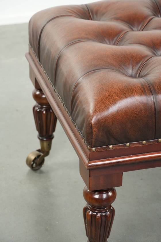 Image 1 of Grote bruine rundleren chesterfield hocker in Engelse stijl met sierlijke poten en messing wieltjes