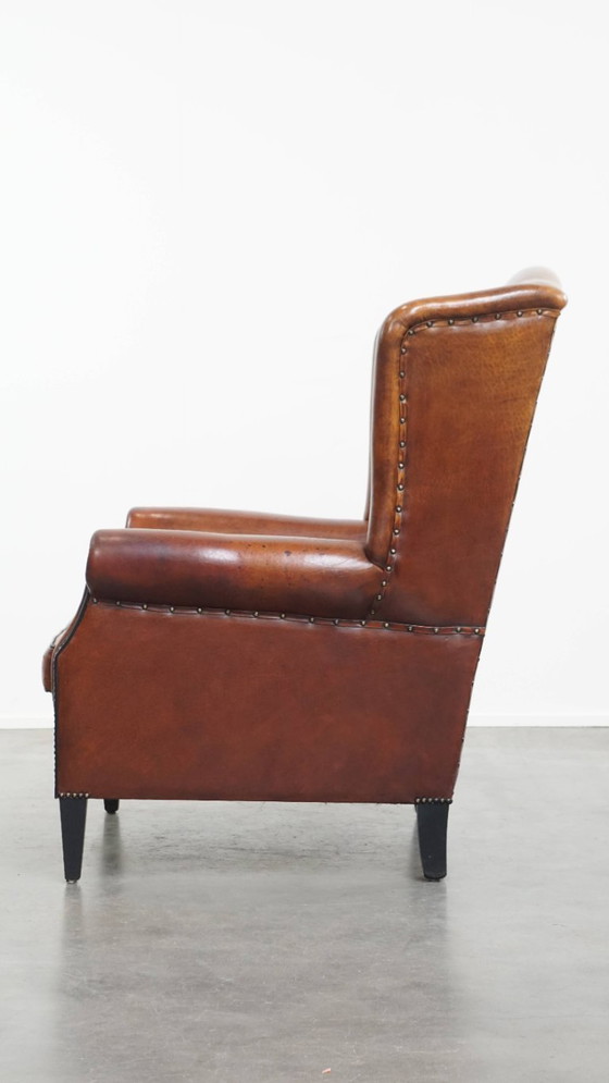 Image 1 of Schapenleren oorfauteuil met een warme kleurstelling en een afwerking met siernagels en zwarte biezen