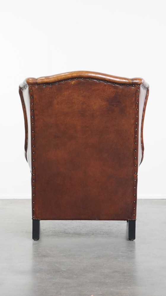 Image 1 of Schapenleren oorfauteuil met een warme kleurstelling en een afwerking met siernagels en zwarte biezen