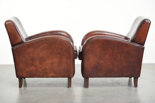 2x dunkel cognacfarbene Schaffellsessel mit abgerundeten Formen und elegantem Design
