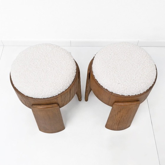 Image 1 of Een paar Art Deco-stijl krukjes van essenhout, bekleed met witte boucléstof.