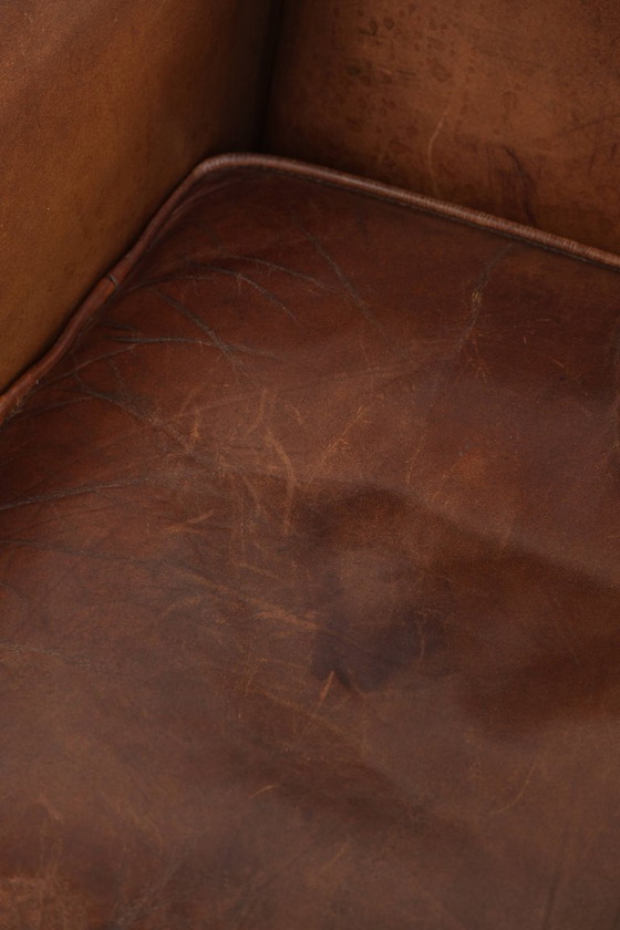 Image 1 of Precioso sillón orejero de piel de oveja marrón oscuro con un aspecto atemporal en un tamaño sutil.