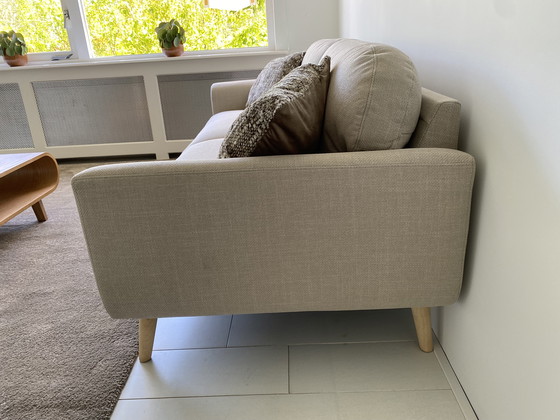 Image 1 of Elegante sofá de 3 plazas con tapicería de tela beige y patas de madera.