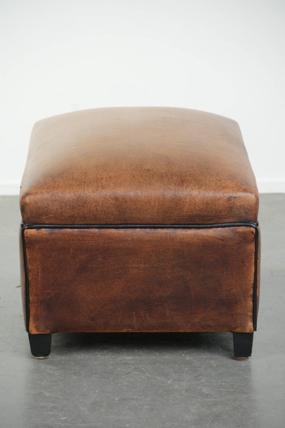 Image 1 of Characterful sheepskin footstool/ottoman with a beautiful patina and finished with black piping.