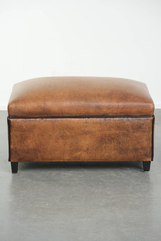 Image 1 of Characterful sheepskin footstool/ottoman with a beautiful patina and finished with black piping.
