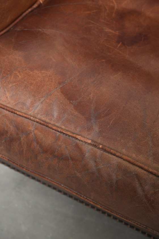 Image 1 of Precioso sillón orejero de piel de oveja marrón oscuro con un aspecto atemporal en un tamaño sutil.