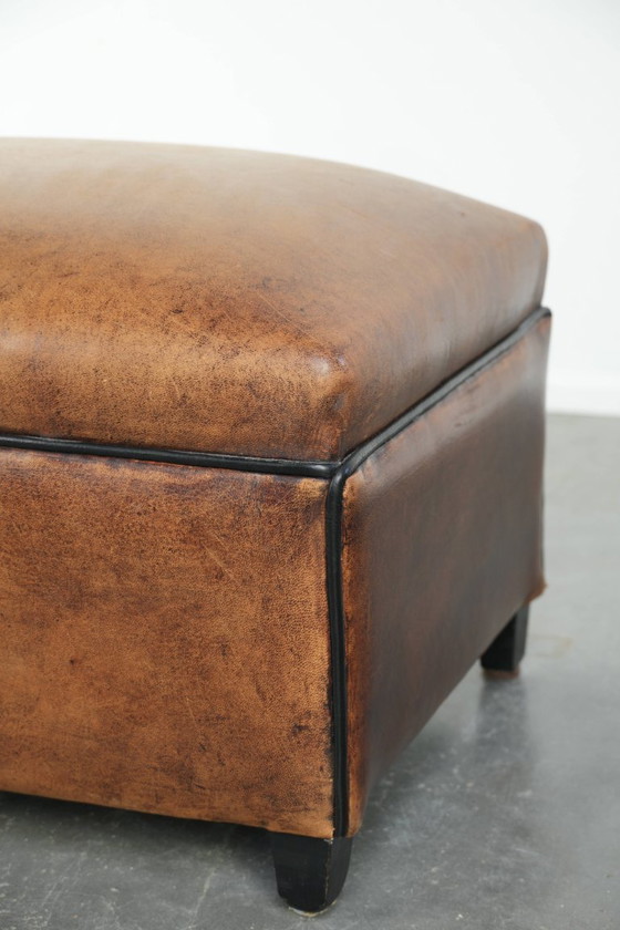 Image 1 of Characterful sheepskin footstool/ottoman with a beautiful patina and finished with black piping.