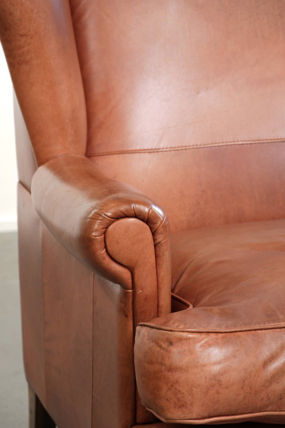 Image 1 of Fauteuil à oreilles en cuir de vachette couleur cognac clair, avec passepoil assorti et un style anglais plein de caractère.