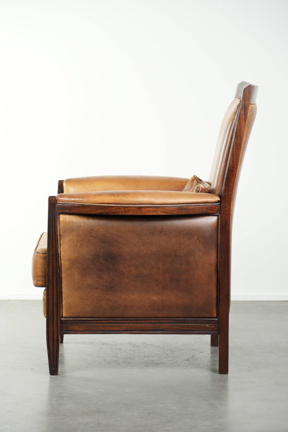 Image 1 of Cómodo sillón de diseño Art Déco en color coñac, fabricado en piel de oveja combinada con madera y con respaldo alto.