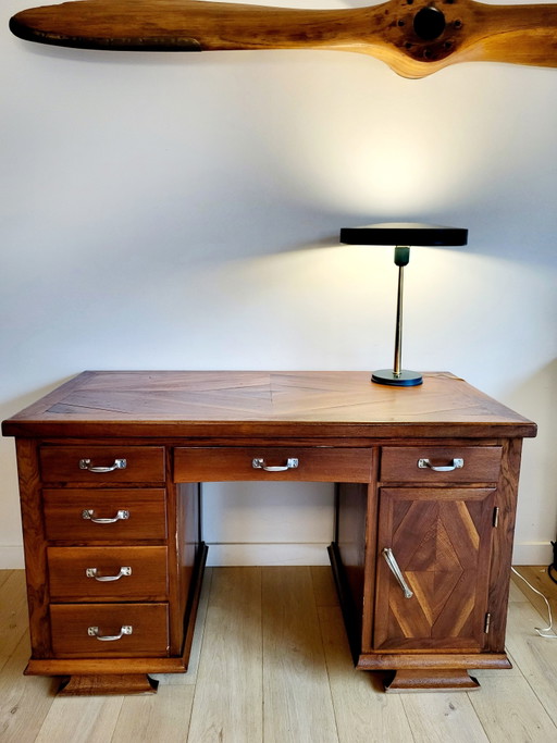Escritorio antiguo con tablero de madera con incrustaciones y tiradores de metal.