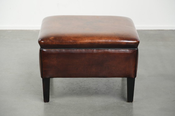 Image 1 of Grote donkerbruine vierkante hocker gemaakt van schapenleer met zwarte biezen