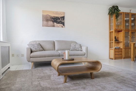 Image 1 of Elegante sofá de 3 plazas con tapicería de tela beige y patas de madera.