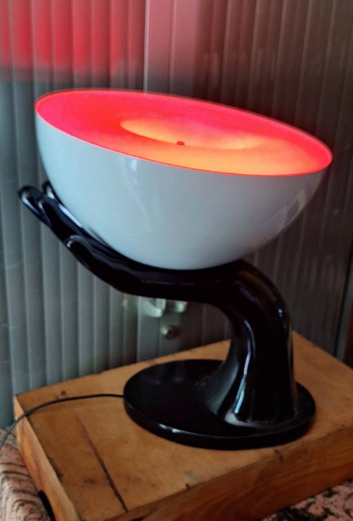 Kare design Tischlampe Josy, schwarze Hand, die warmes Licht spendet.
