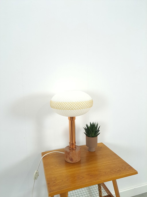 Lámpara de mesa con base de mármol y pantalla de cobre y cristal lechoso.