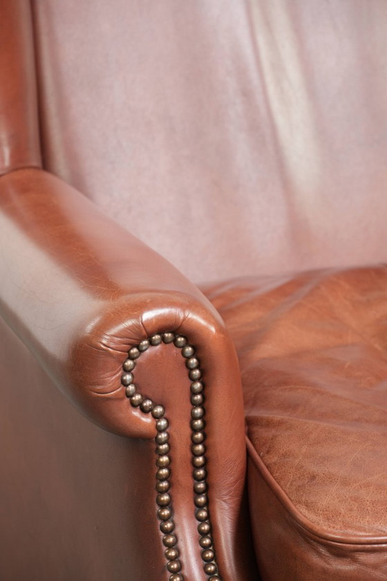 Image 1 of Comoda poltrona a orecchioni in pelle bovina color cognac in stile inglese.
