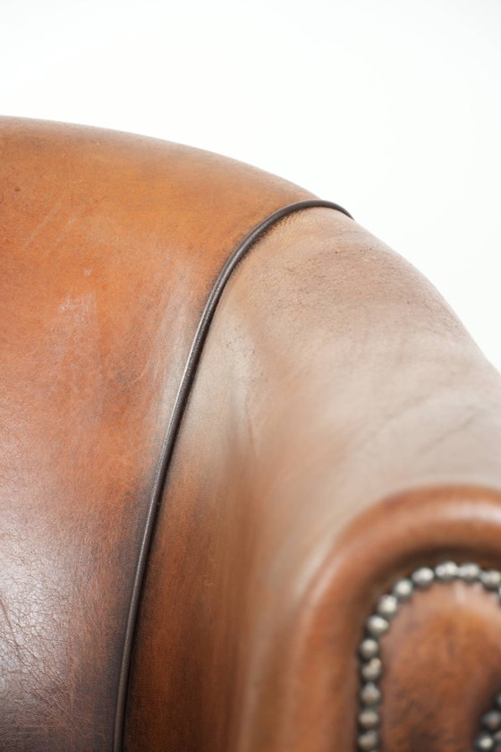 Image 1 of Schapenleren clubfauteuil met een mooie patina en een verfijnde afwerking met zwarte biezen