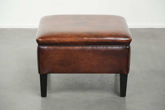 Image 1 of Grote donkerbruine vierkante hocker gemaakt van schapenleer met zwarte biezen