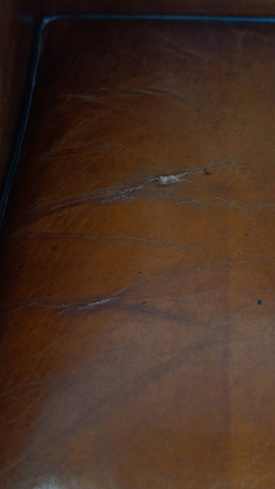 Image 1 of Schapenleren oorfauteuil met een warme kleurstelling en een afwerking met siernagels en zwarte biezen