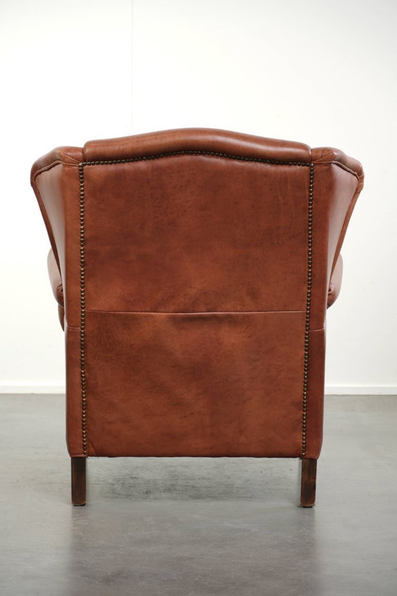 Image 1 of Fauteuil à oreilles en cuir de vachette couleur cognac clair, avec passepoil assorti et un style anglais plein de caractère.