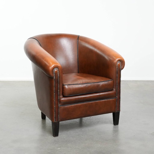 Fauteuil club de style anglais en cuir de vachette, orné de clous décoratifs et d'un passepoil noir.