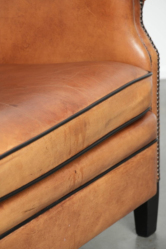 Image 1 of Amplio sillón club de estilo inglés, tapizado en piel de oveja, con acabado de clavos decorativos y ribetes negros.