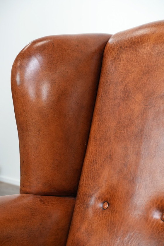 Image 1 of Grote oorfauteuil gemaakt van schapenleer met zwarte biezen en siernagels