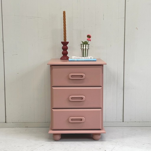Cómoda vintage de madera color rosa salmón con mesita de noche.
