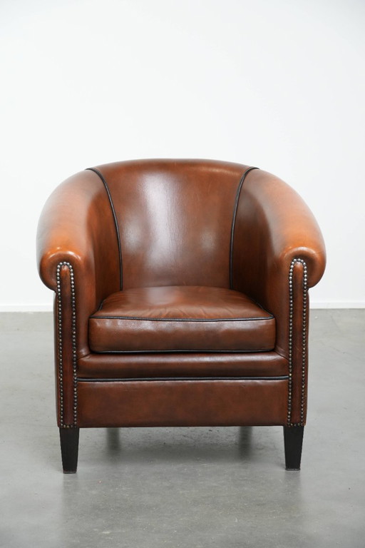 Fauteuil club de style anglais en cuir de vachette, orné de clous décoratifs et d'un passepoil noir.