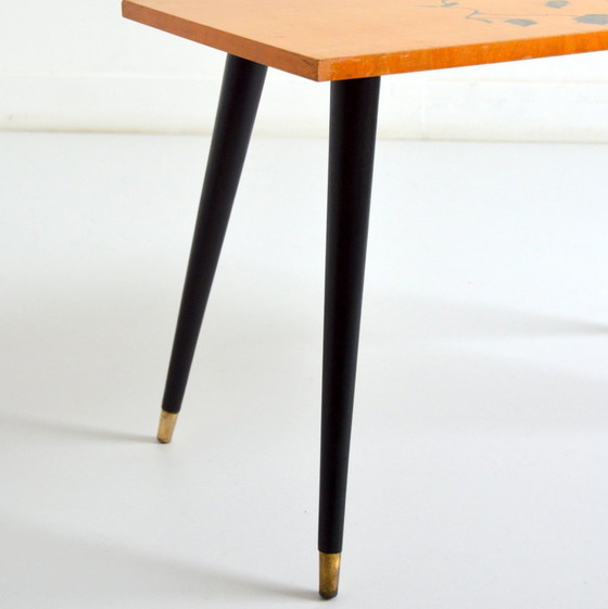 Image 1 of Pretty coffee table from the 50s/60s.  Decorated with a bird on a branch.  Black brass-finish tapered legs.  L 80/ W 40/ H 51