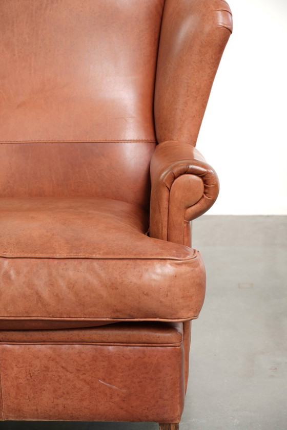 Image 1 of Fauteuil à oreilles en cuir de vachette couleur cognac clair, avec passepoil assorti et un style anglais plein de caractère.