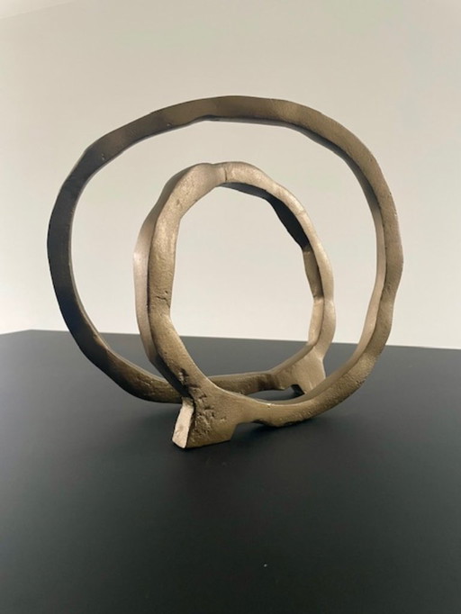 Escultura de diseño con forma de anillo abierto en oro mate.