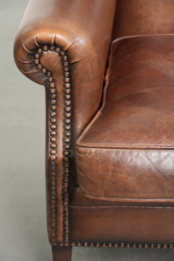 Image 1 of Precioso sillón orejero de piel de oveja marrón oscuro con un aspecto atemporal en un tamaño sutil.