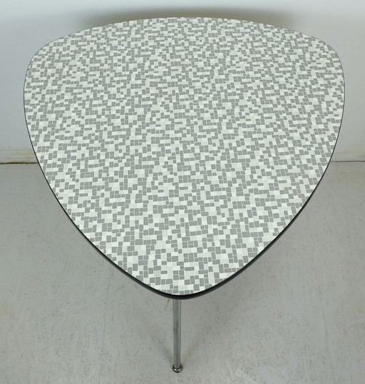 Mesa de centro de tres patas de los años 50 con tablero de formica y patas cromadas inclinadas.