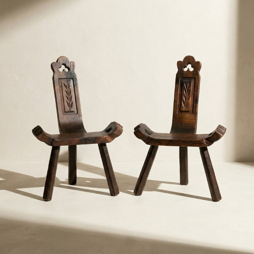 Een paar lage, brutalistische stoelen met drie poten, gemaakt van massief hout, midden 20e eeuw.