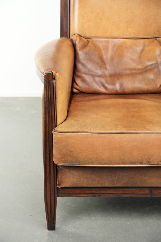 Image 1 of Cómodo sillón de diseño Art Déco en color coñac, fabricado en piel de oveja combinada con madera y con respaldo alto.