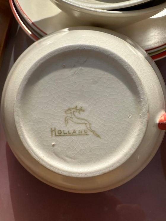 Image 1 of Set van 7 aardewerken kopjes, 5 schotels en 1 melkkan. Gemerkt met afbeelding van een springend hert en het woord 'Holland'.    