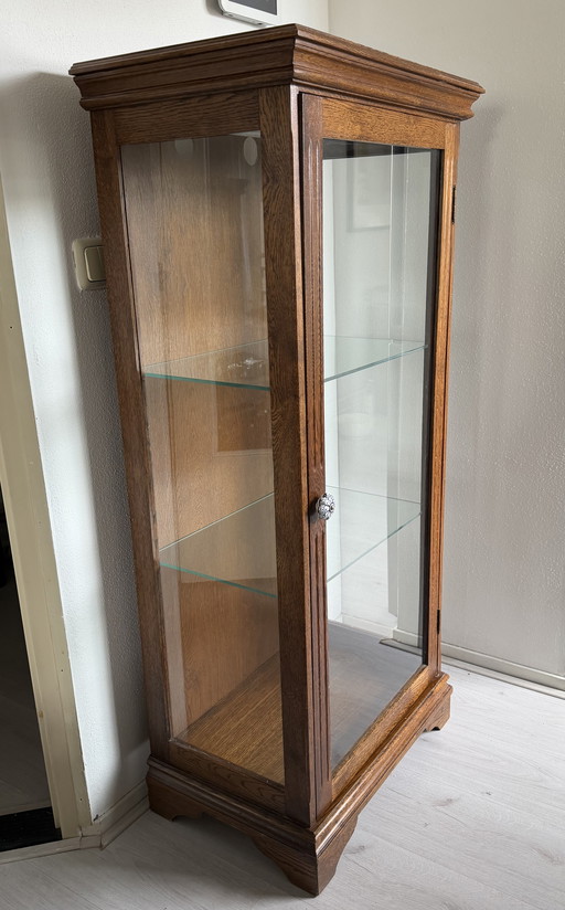 Houten vitrinekast met glazen deur en planken.