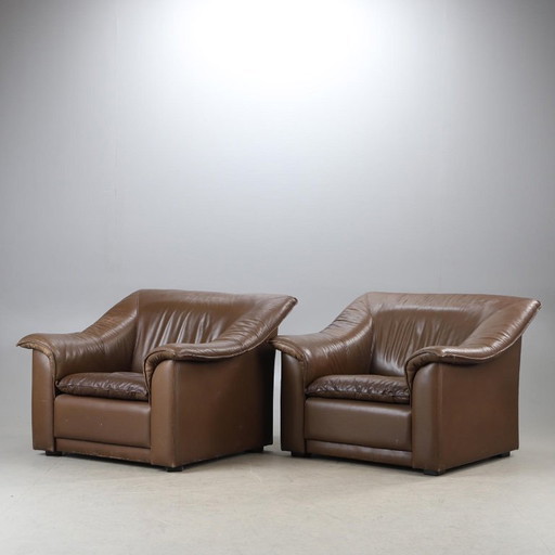 Pair of mid‑century brown leather club armchairs in good condition with small signs of aging and blemishes