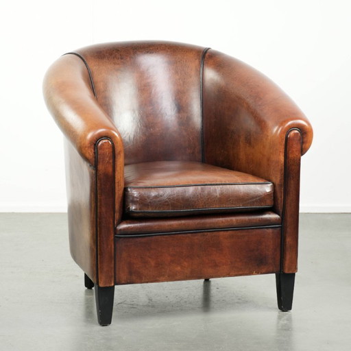 Mooie en karaktervolle schapenleren clubfauteuil met mooie diepe warme kleuren, zwarte biezen en een comfortabele zit