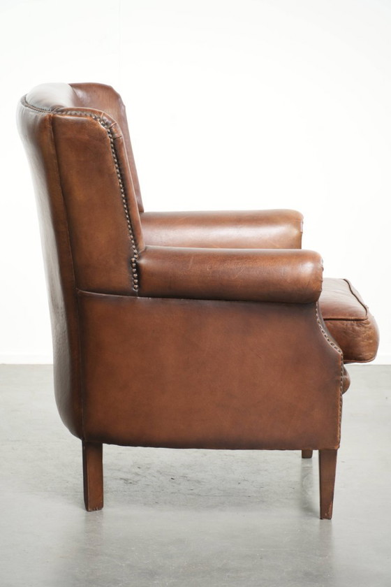 Image 1 of Precioso sillón orejero de piel de oveja marrón oscuro con un aspecto atemporal en un tamaño sutil.