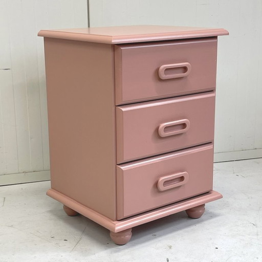 Cómoda vintage de madera color rosa salmón con mesita de noche.