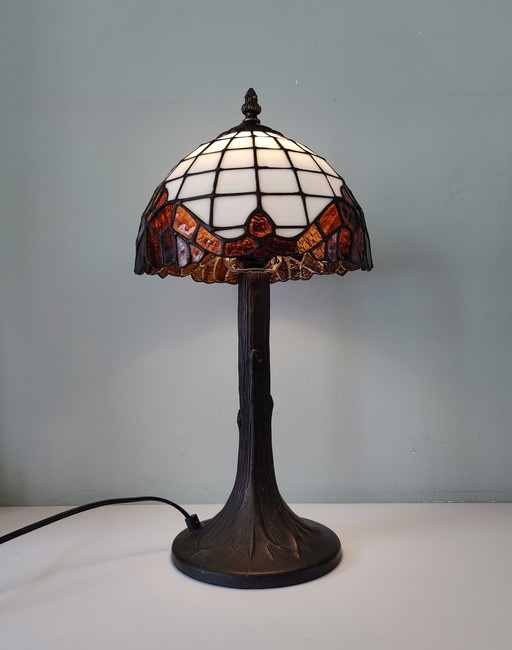 Lámpara de mesa estilo Tiffany con pantalla de vidrieras y base de bronce.