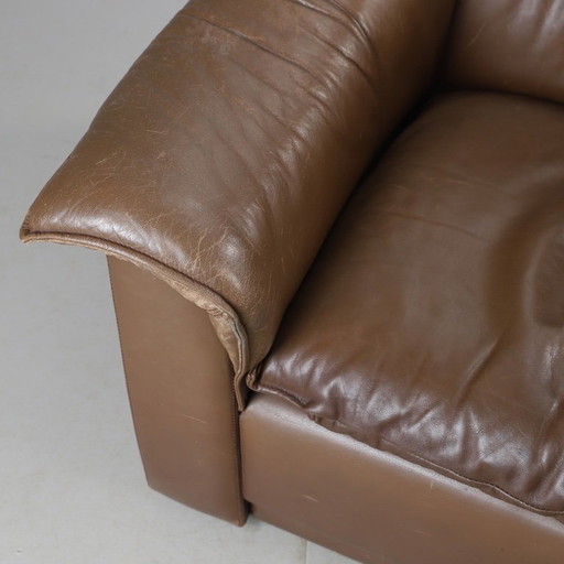 Pair of mid‑century brown leather club armchairs in good condition with small signs of aging and blemishes