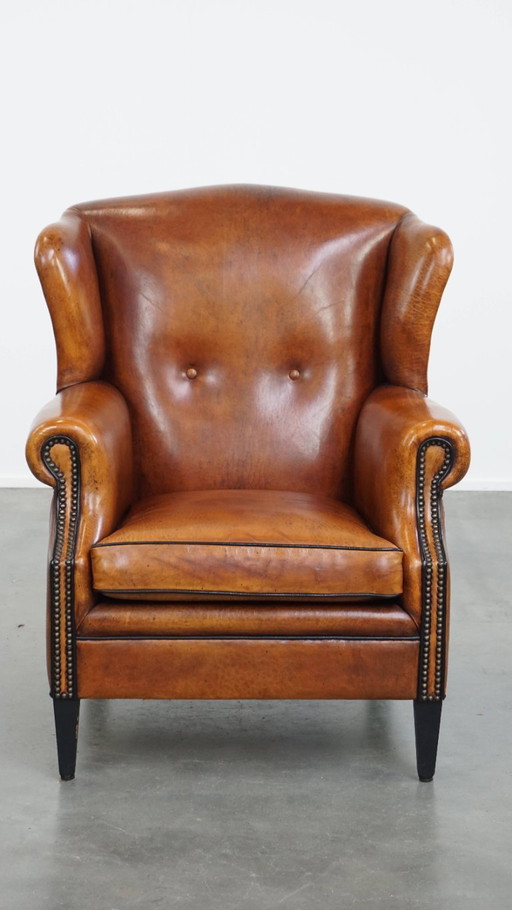 Comfortabele schapenleren oorfauteuil met een prachtige warme kleurstelling en een afwerking met stiksels en zwarte biezen