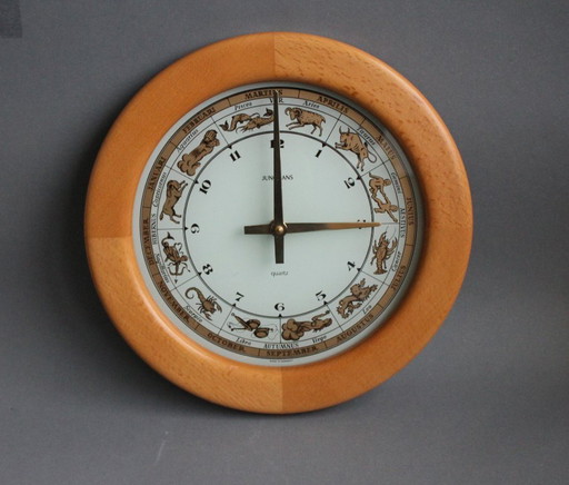 Horloge murale vintage Junghans avec boîtier en bois et signe du zodiaque sur un cadran en verre.